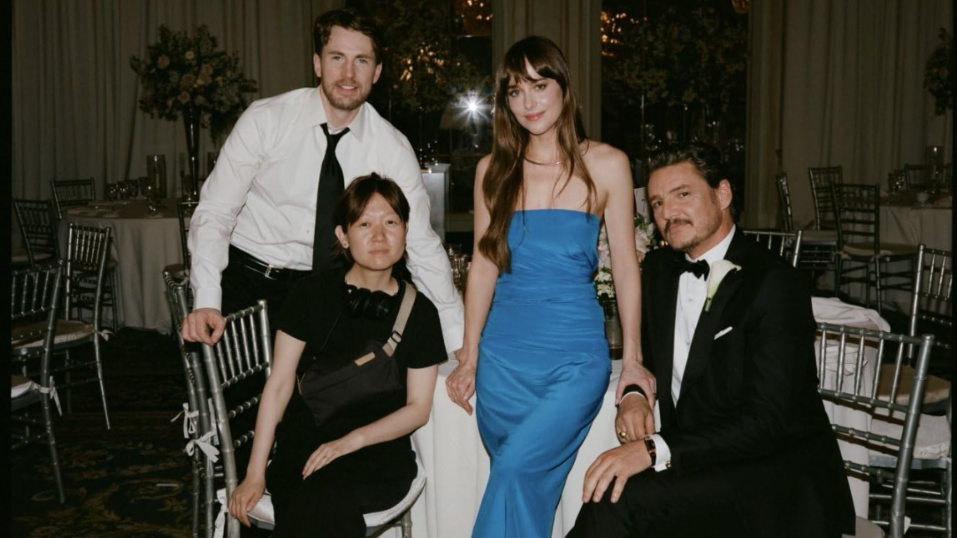 Actorii Dakota Johnson, Chris Evans și Pedro Pascal stând în ținute de seară la o masă albă