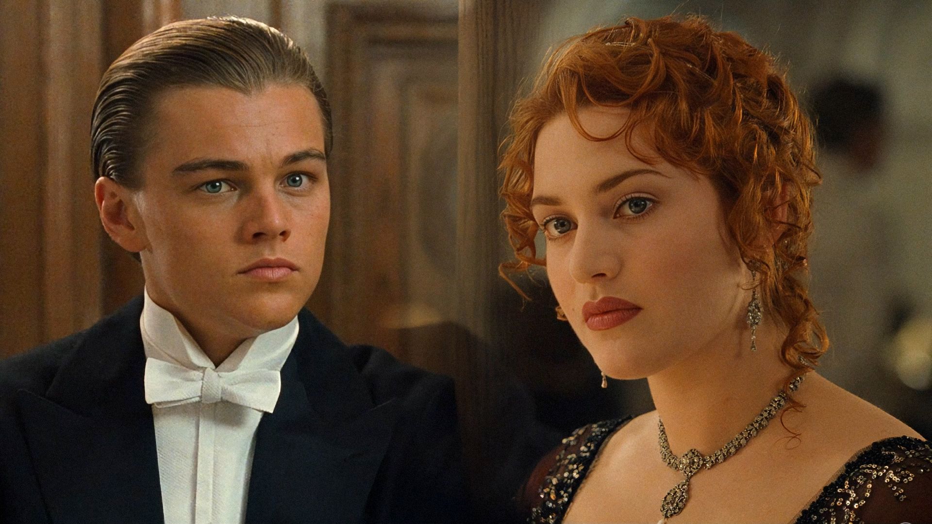 Actorul Leonardo DiCaprio în smoking și actrița Kate Winslet într-o rochie neagră stând pe un fundal maro