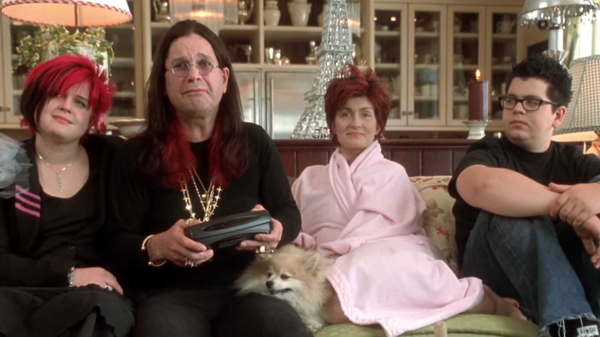 Cântărețul Ozzy Osbourne într-un costum negru cu lanțuri stă pe canapea cu soția și copiii săi