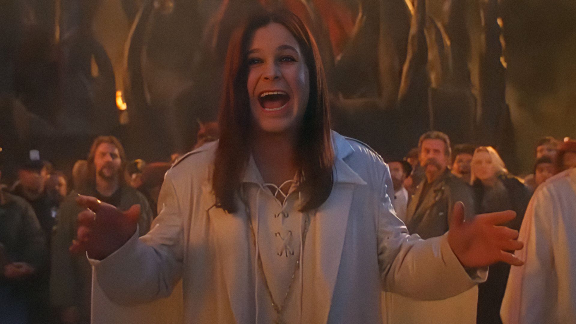 Cântărețul Ozzy Osbourne într-o jachetă albă își întinde brațele și zâmbește