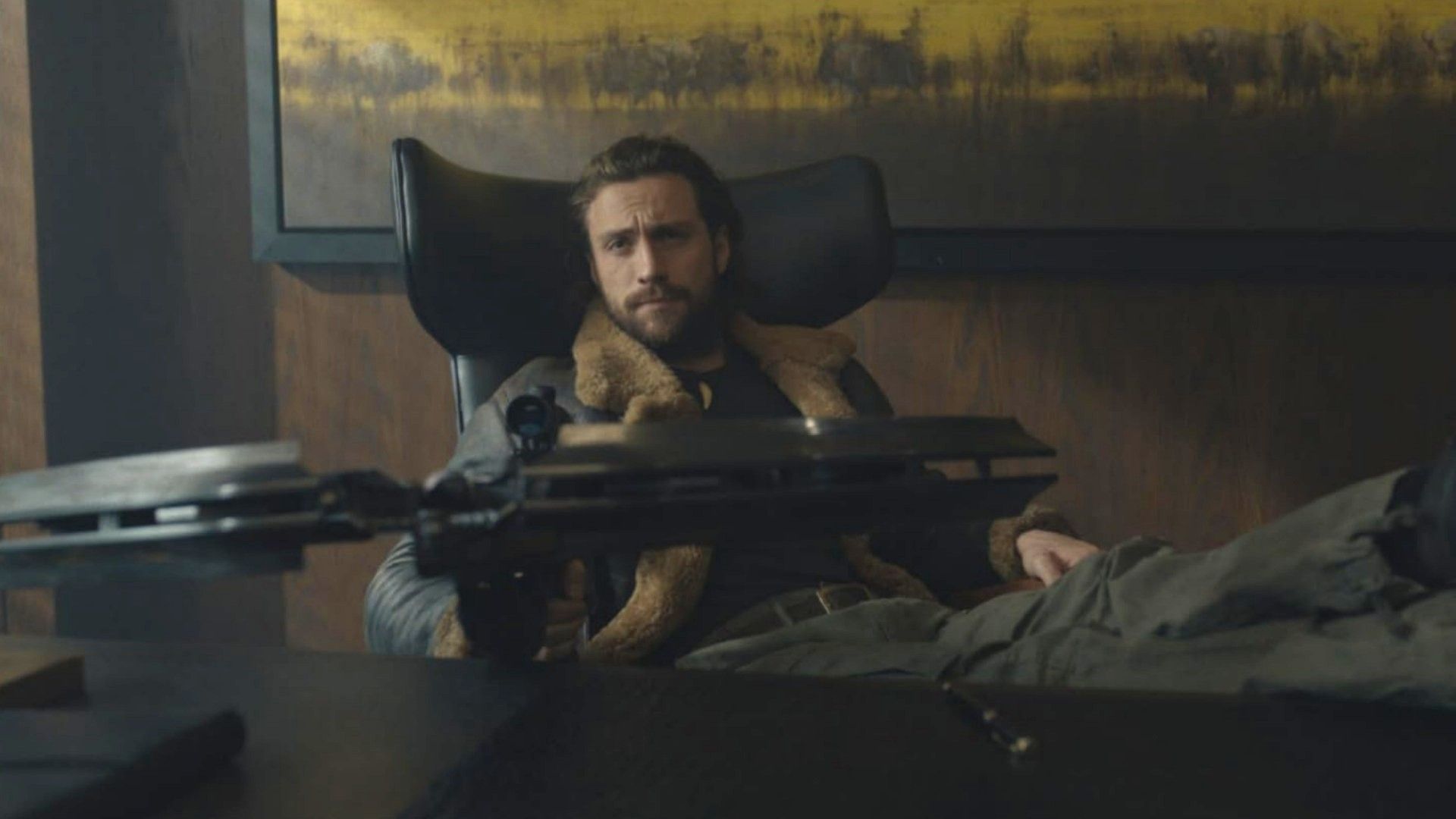 Actorul Aaron Taylor-Johnson stă la o masă cu o arbaletă în mâini