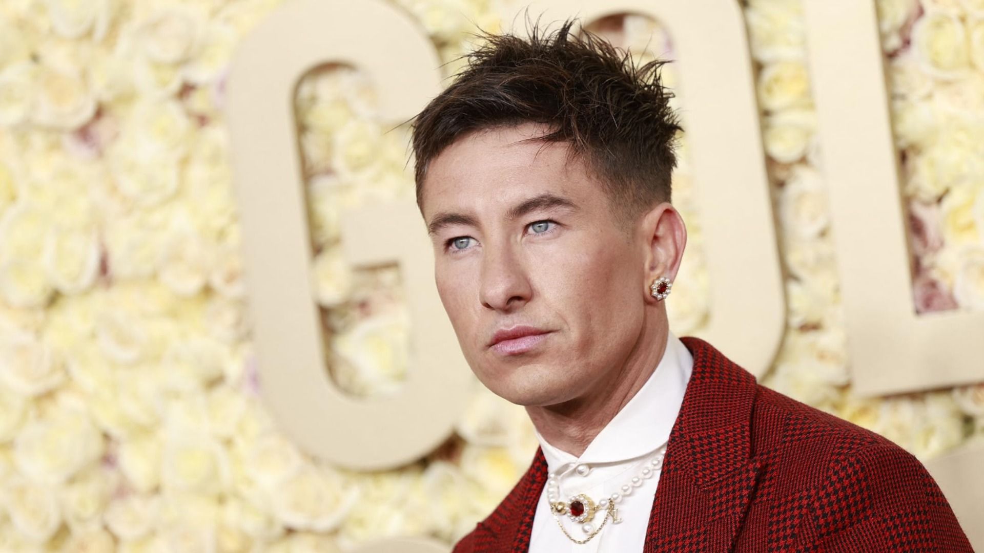 Actorul Barry Keoghan într-o jachetă roșie cu un cercel, stând pe un fundal galben