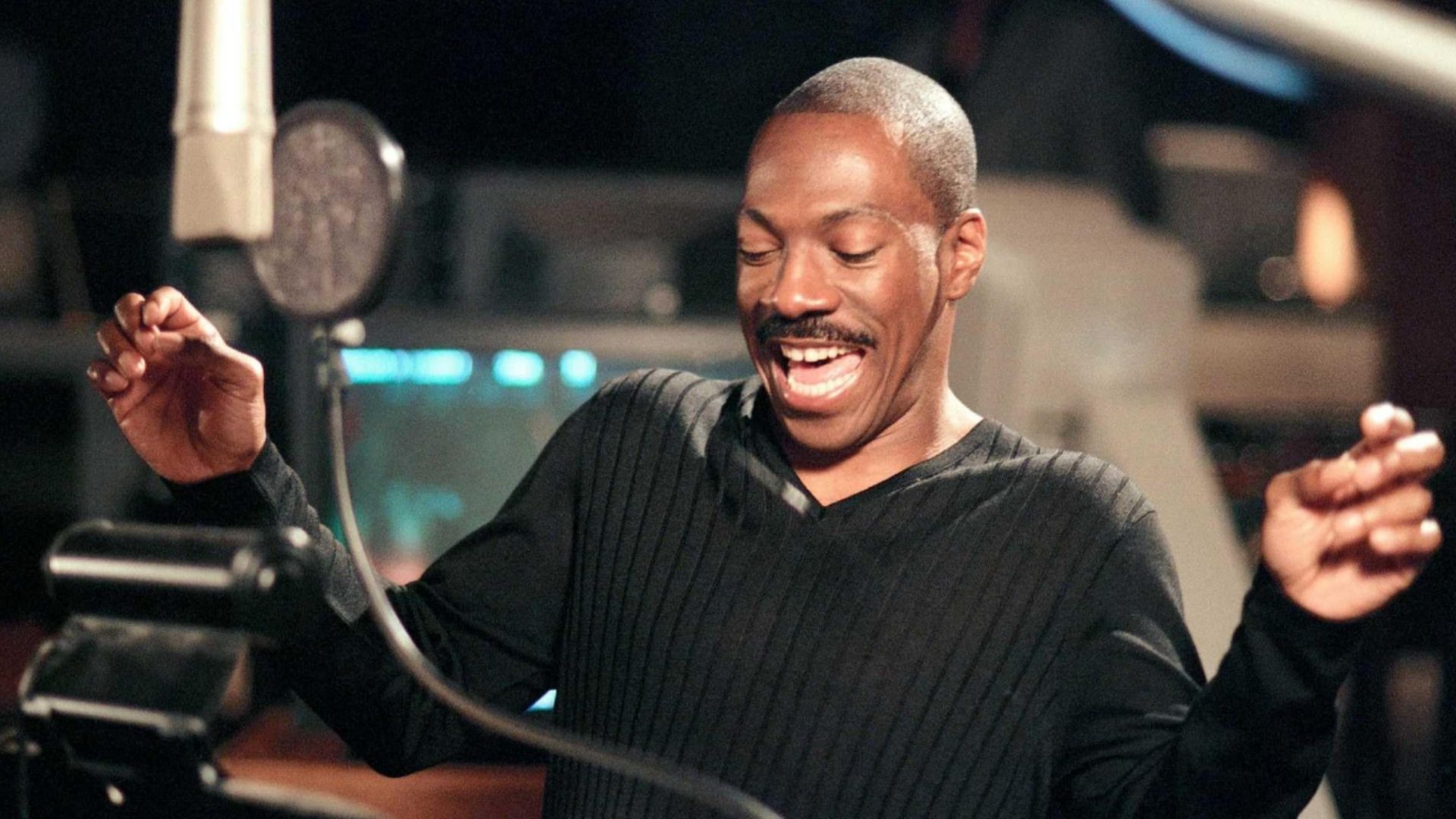 Actorul Eddie Murphy într-un pulover negru stă la microfon și zâmbește