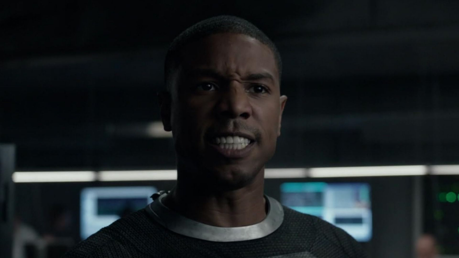 Actorul Michael B. Jordan într-un costum gri, arătând furios pe un fundal neclar