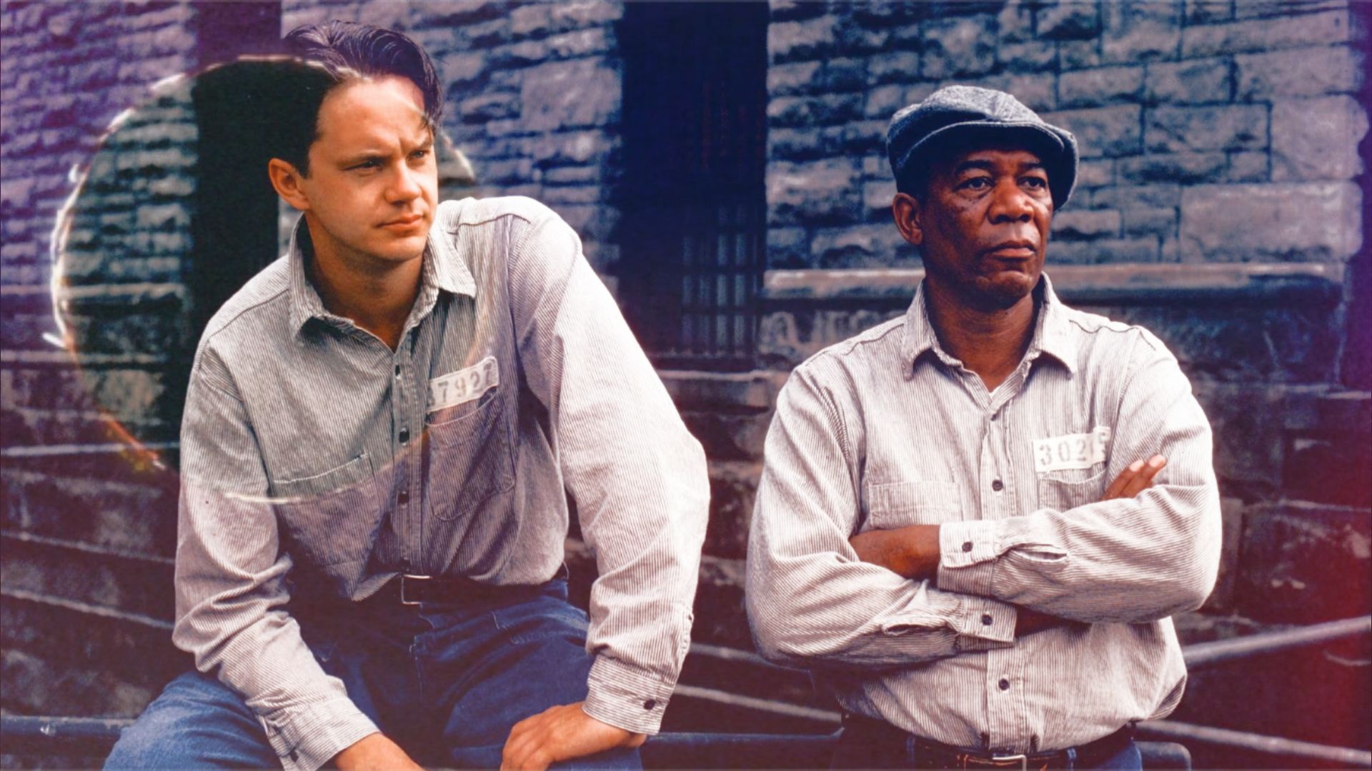 Actorii Tim Robbins și Morgan Freeman în uniforme de închisoare stând lângă un zid de piatră