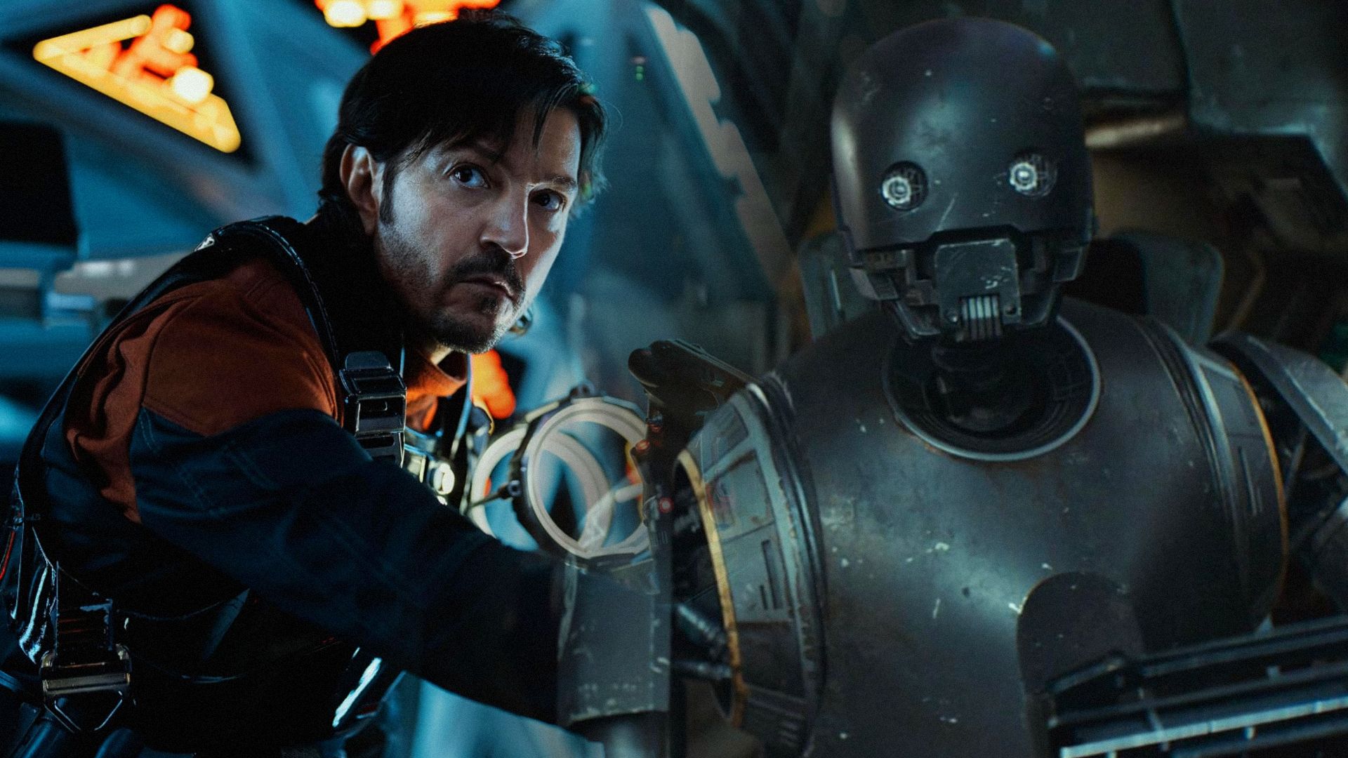 Actorul Diego Luna în haine negre în interiorul unei nave spațiale cu un robot gri închis în apropiere