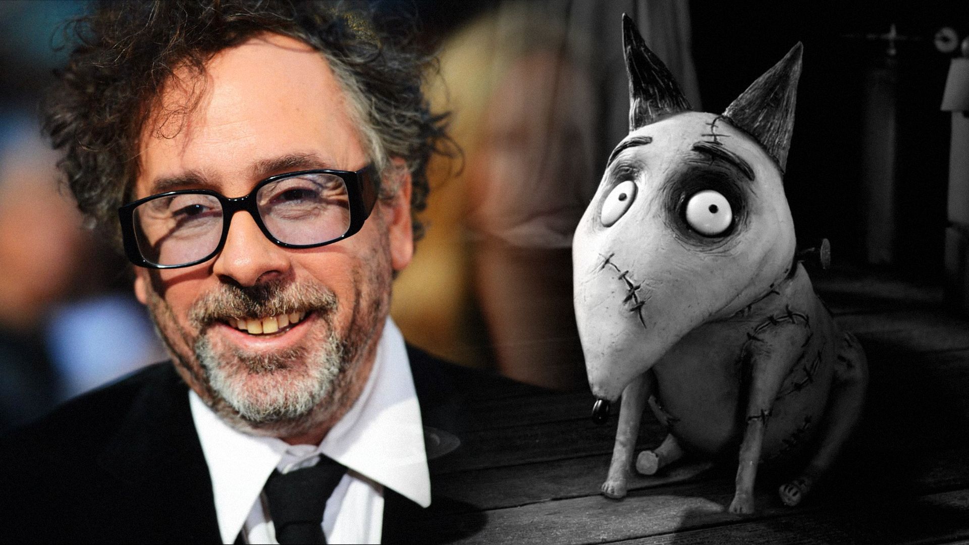 Regizorul Tim Burton în jachetă neagră și ochelari, cu un câine gri lângă el