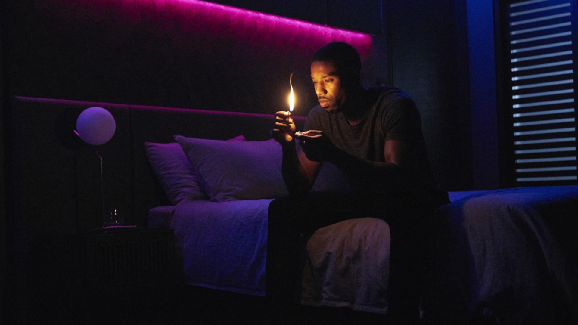 Actorul Michael B. Jordan stă pe un pat cu un chibrit în mâini