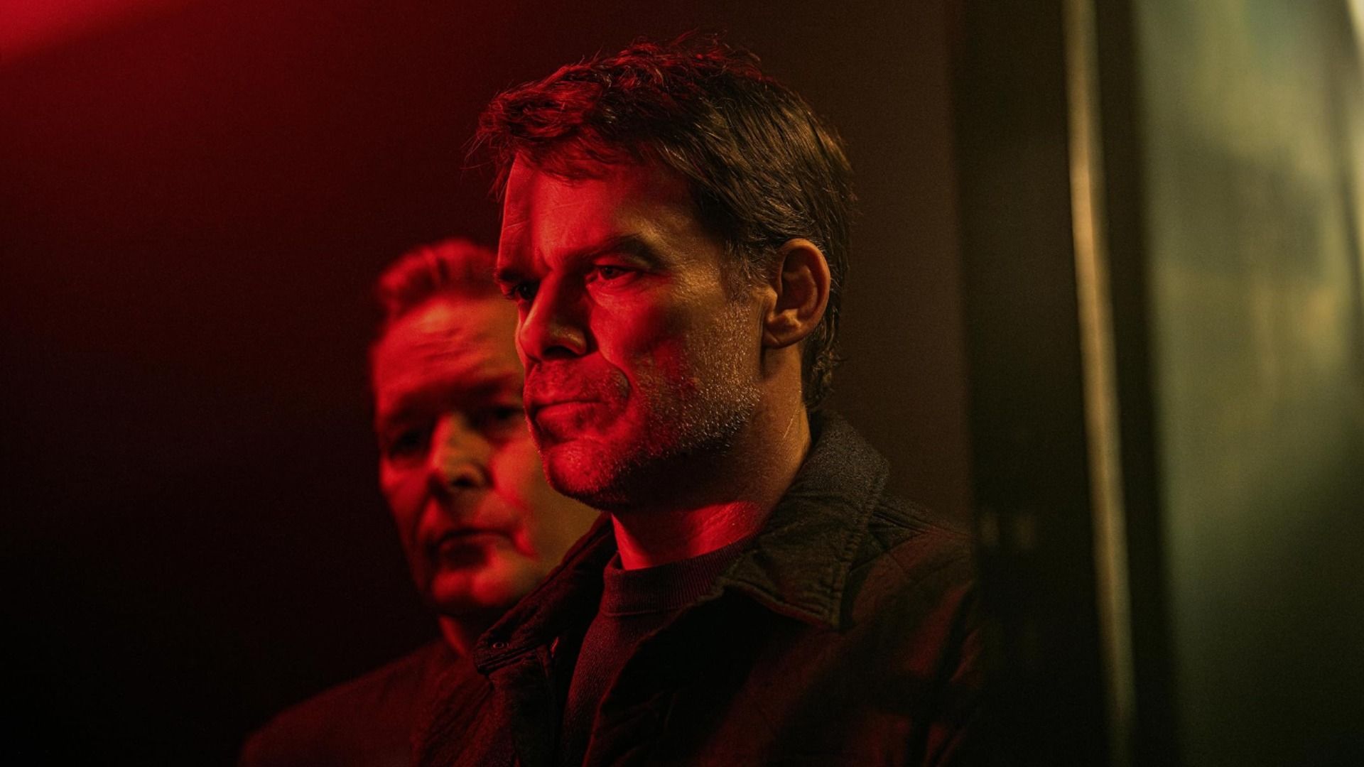 Actorul Michael C. Hall stă în profil într-o lumină roșie cu partea unei fețe de bărbat vizibilă în spatele lui