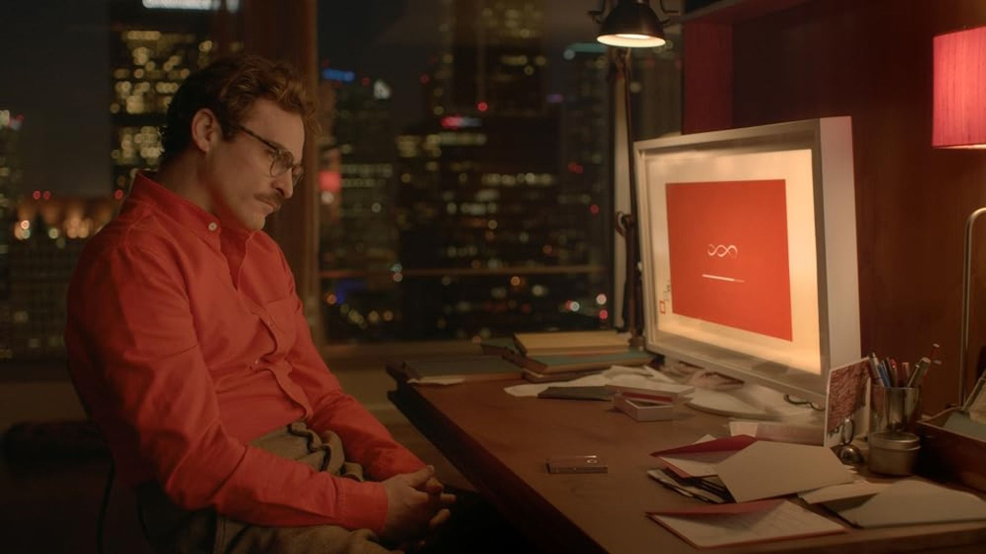 Actorul Joaquin Phoenix într-o cămașă roșie stă la o masă cu un computer pe ea