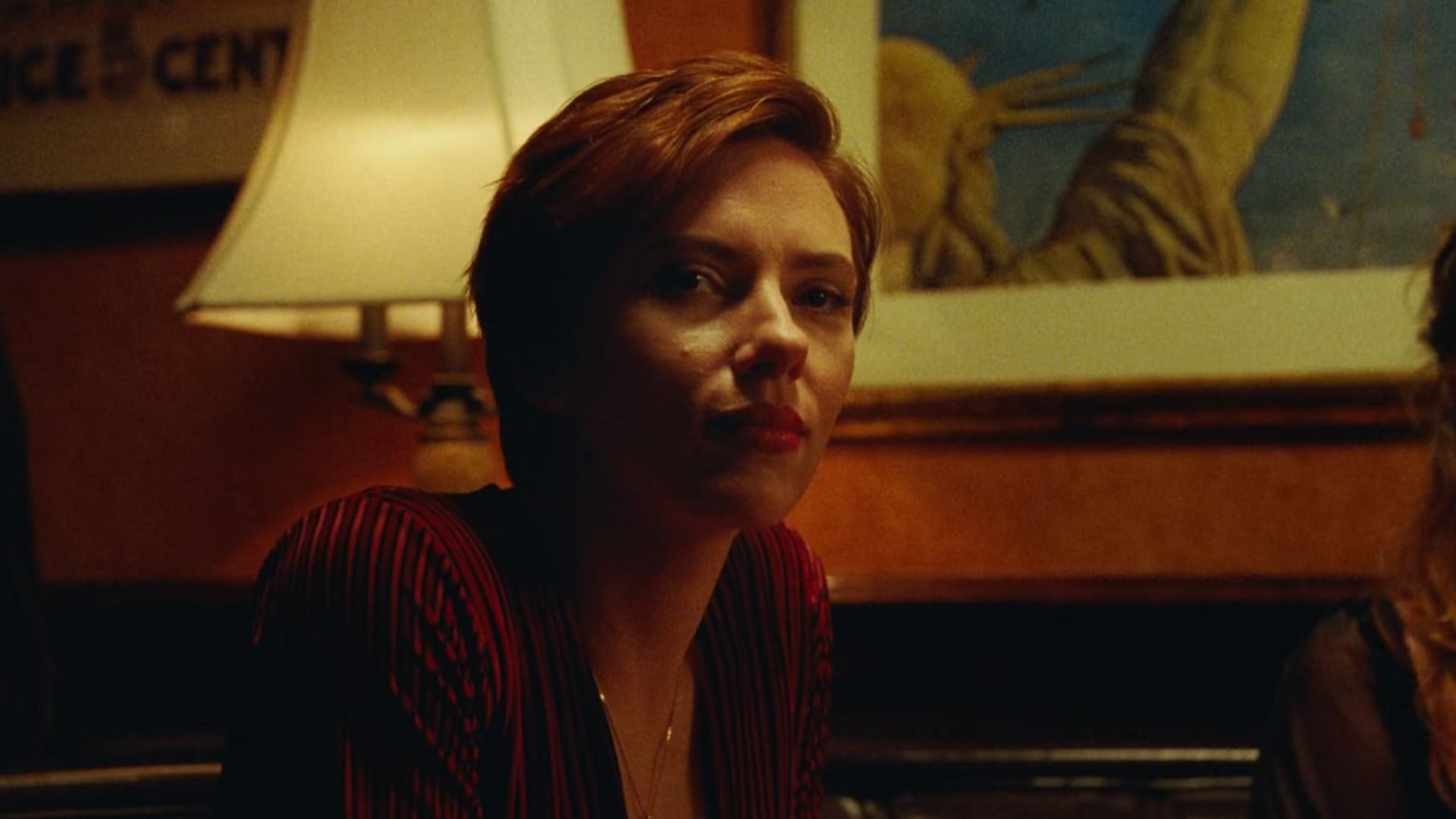 Actrița Scarlett Johansson într-o bluză roșie stă lângă o lampă