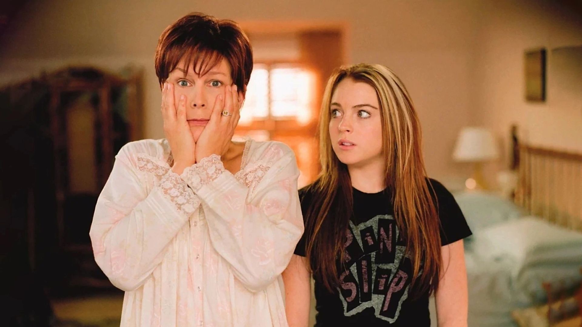 Jamie Lee Curtis în pijamale, șocată cu mâinile acoperindu-și fața în timp ce Lindsay Lohan se uită la ea surprinsă