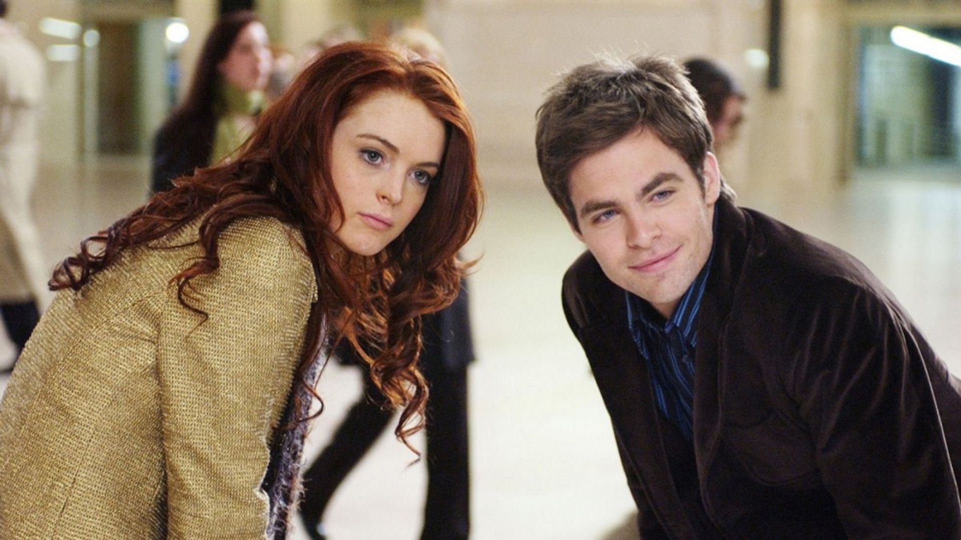 Lindsay Lohan și Chris Pine stau unul lângă altul, aplecându-se înainte într-o cameră aglomerată