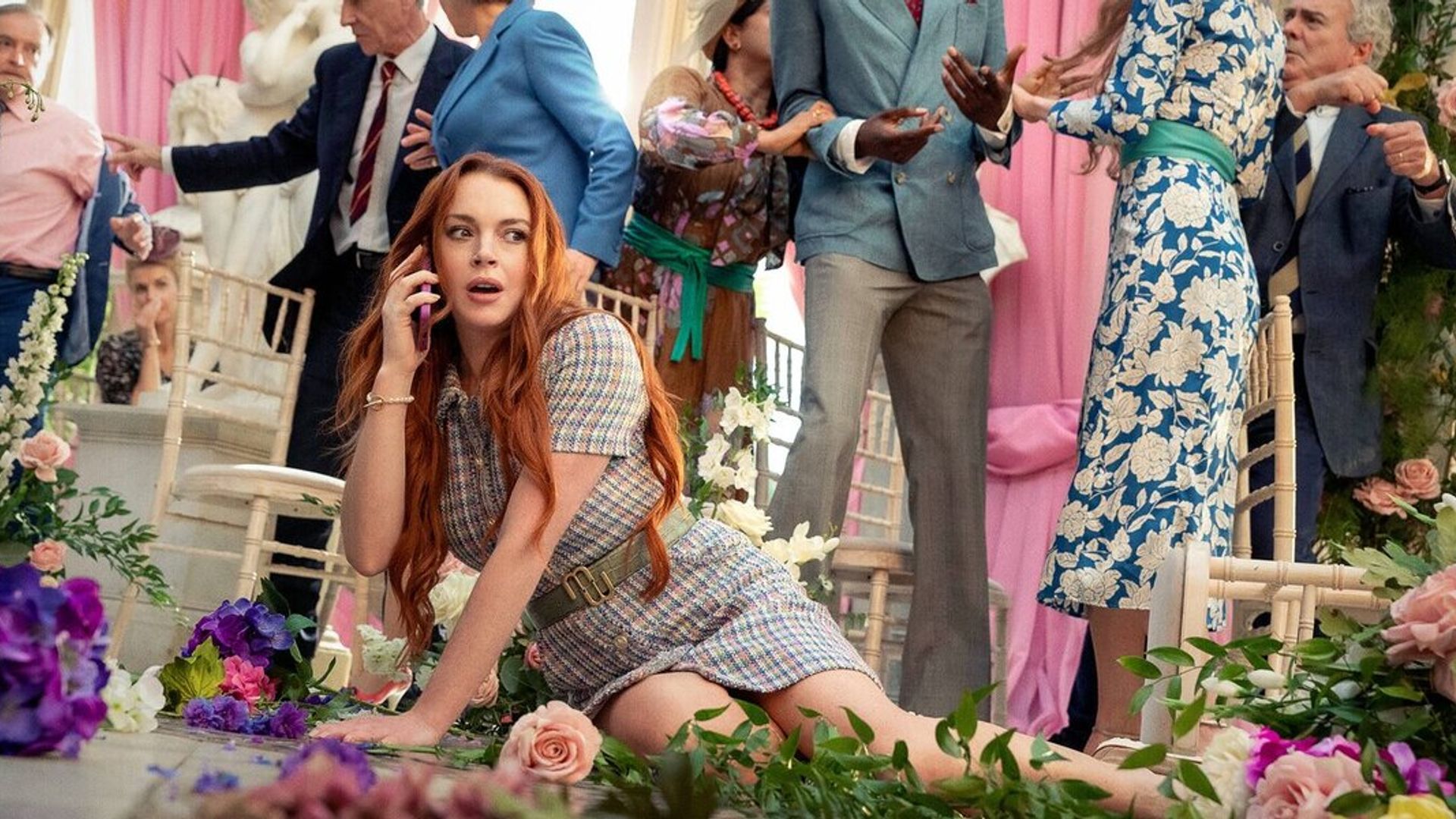 Lindsay Lohan căzută pe podea printre flori în timp ce vorbește la telefon cu haosul ceremoniei de nuntă în fundal