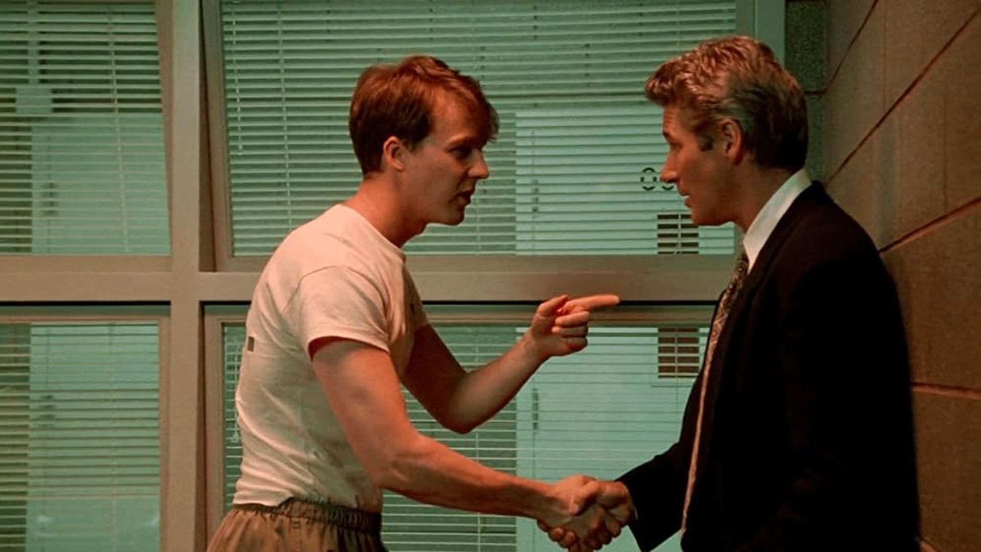 Edward Norton în tricou dând mâna cu Richard Gere în costum, arătându-l cu degetul