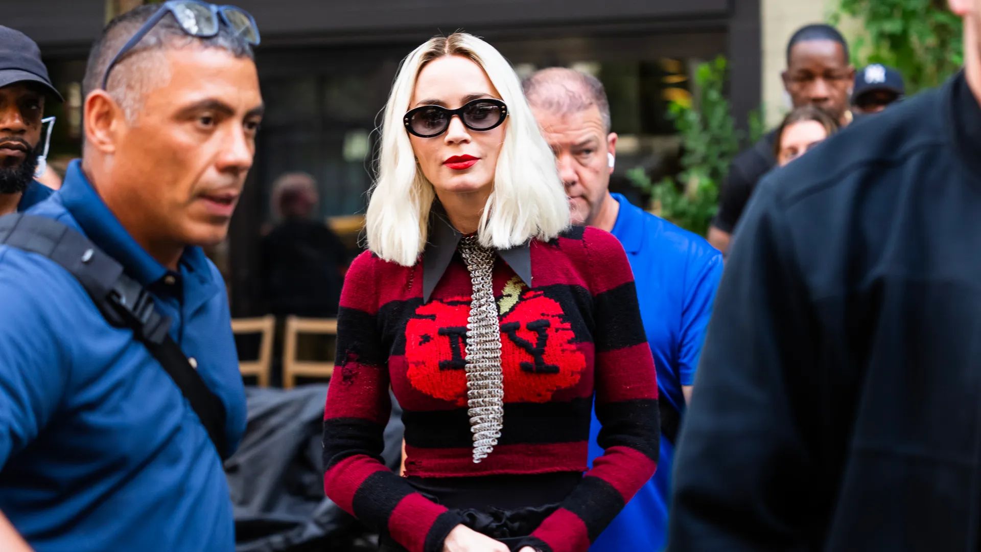 Emily Blunt cu bob blond platină într-un pulover roșu cu inscripția NY