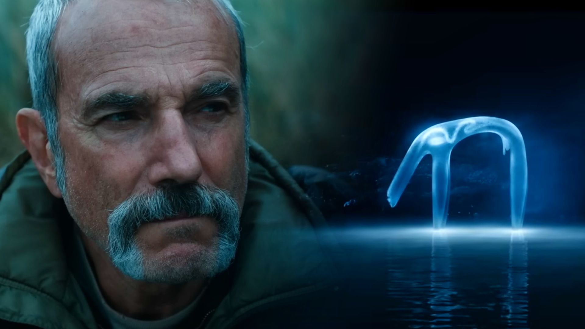 Actorul Daniel Day-Lewis într-o jachetă verde și o creatură albăstruie translucidă stând pe apă