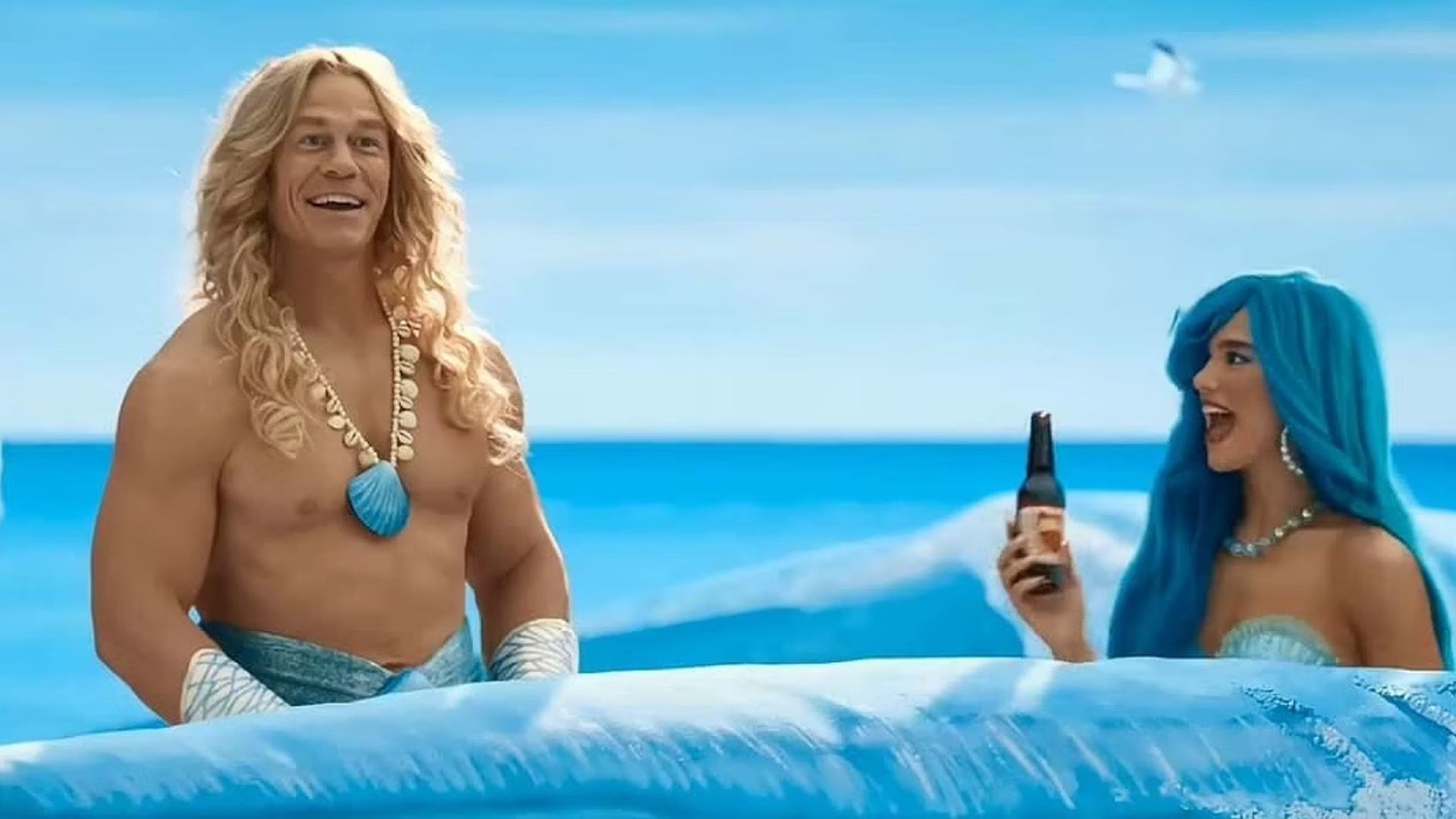 John Cena și Dua Lipa în costume de sirenă înotând prin valuri pictate