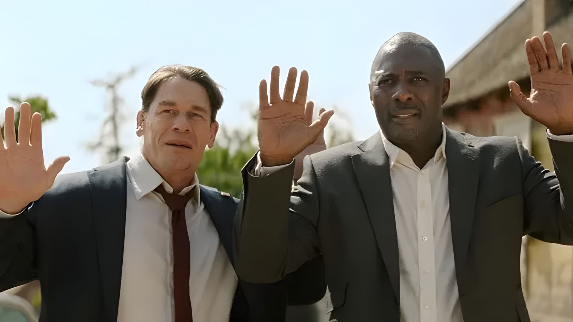 John Cena și Idris Elba în costume ridicând mâinile în sus, scenă dintr-un film de acțiune