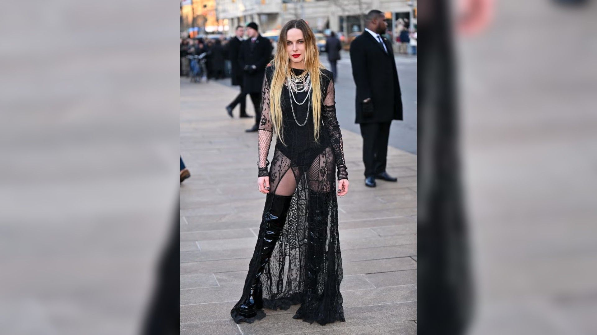 Rebecca Ferguson pozează în aer liber într-o rochie lungă neagră transparentă cu dantelă și cizme înalte din piele lacuită.