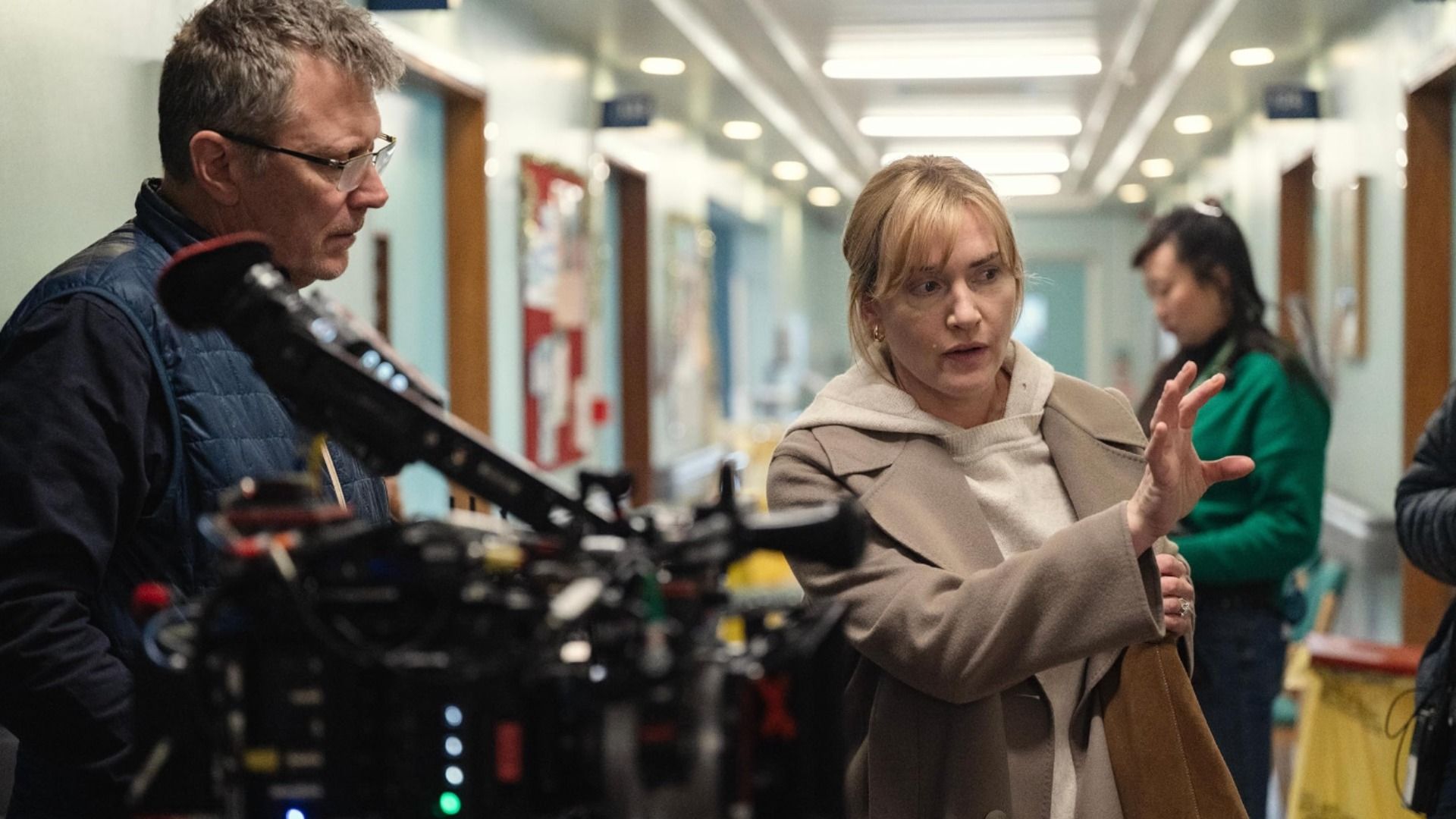 Actrița Kate Winslet într-un palton bej dă indicații unui bărbat cu o cameră