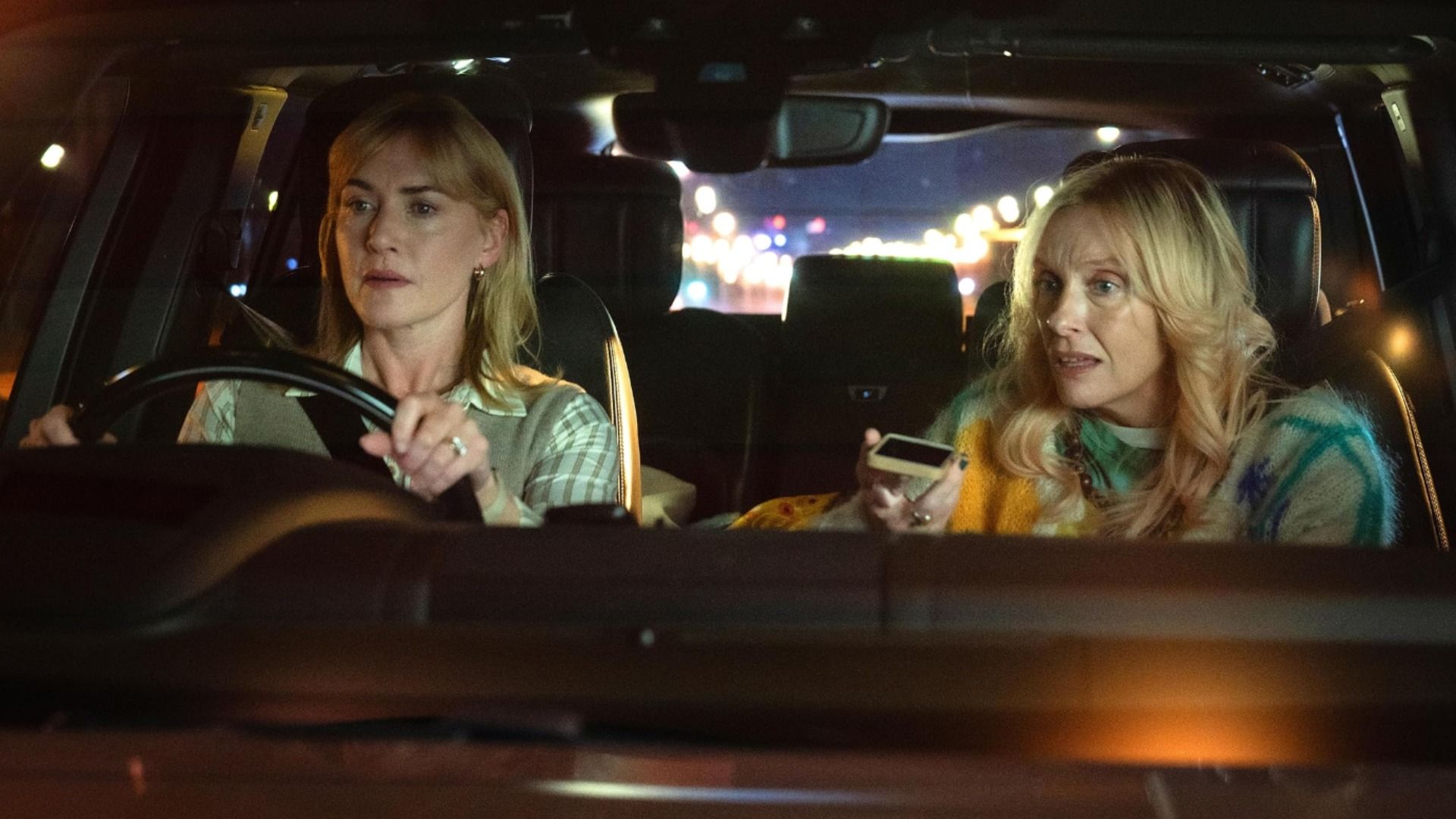 Actrița Kate Winslet stă la volanul unei mașini în timp ce actrița Toni Collette vorbește la telefon lângă ea