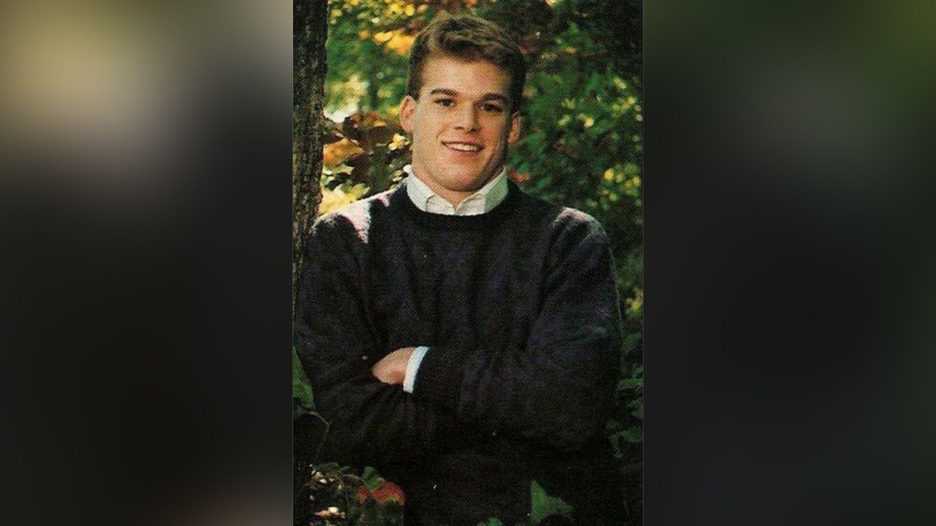 Michael C. Hall tânăr stă cu brațele încrucișate pe piept, zâmbind larg