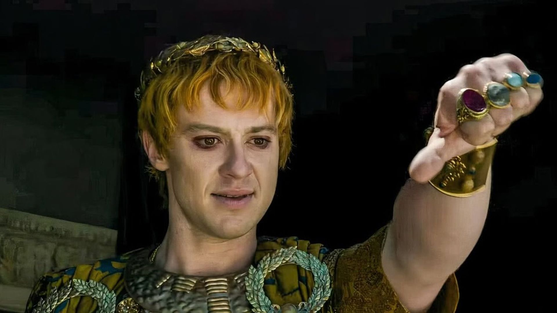 Joseph Quinn în machiaj și costum de împărat roman făcând gestul cu degetul în jos