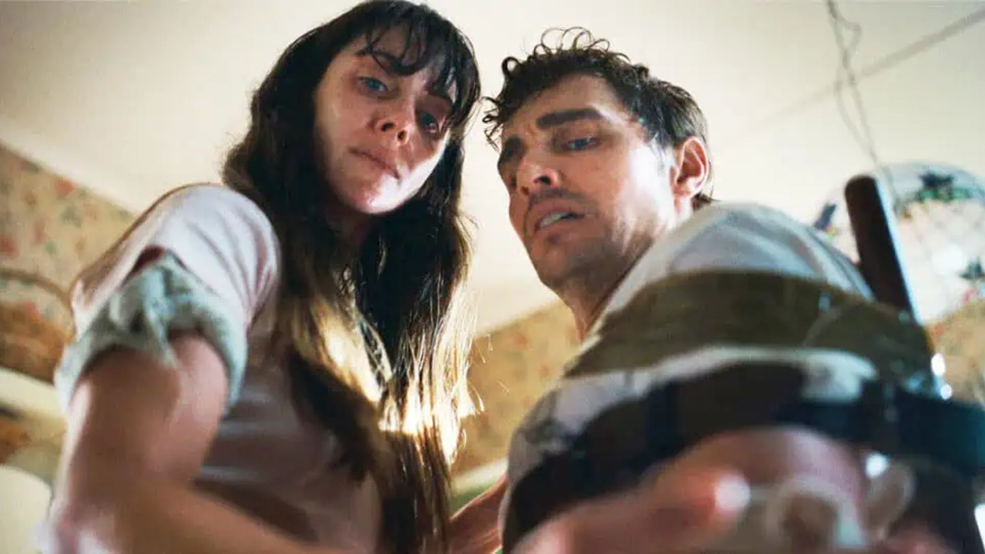 Dave Franco și Alison Brie se uită în jos spre cameră cu expresii obosite pe față