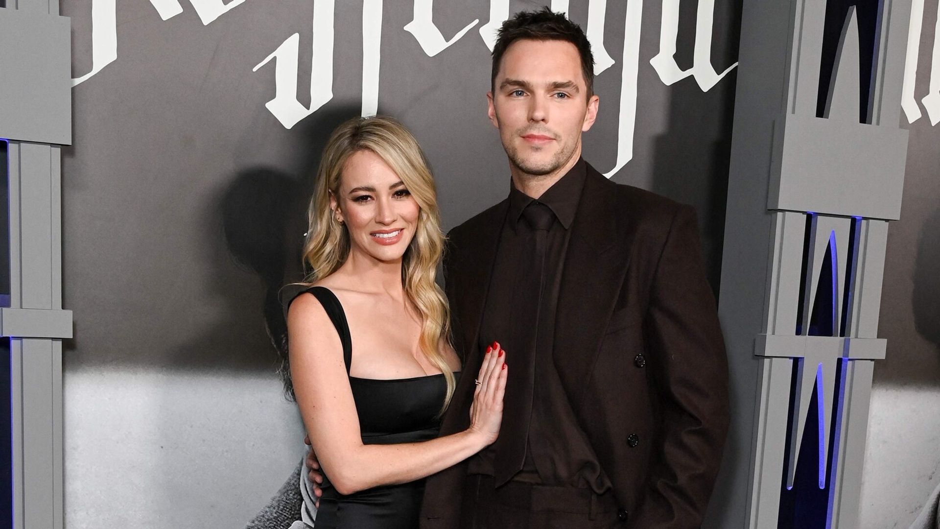 Nicholas Hoult într-un costum întunecat și Bryana Holly într-o rochie neagră pozează împreună pe covorul roșu
