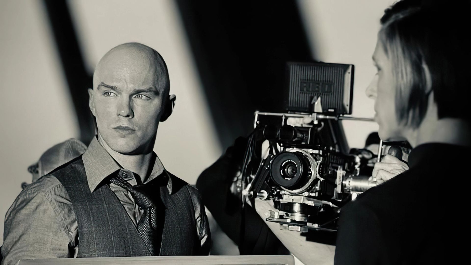 Nicholas Hoult în vestă și cravată stă lângă o cameră de filmat profesională pe un platou de film