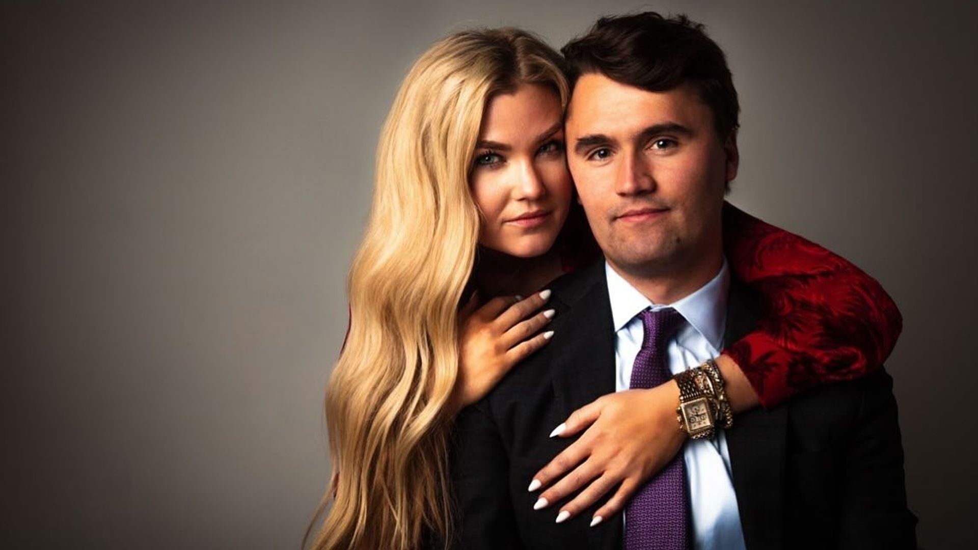 Charlie Kirk și Erica Frantzve se îmbrățișează în fața camerei pe un fundal întunecat