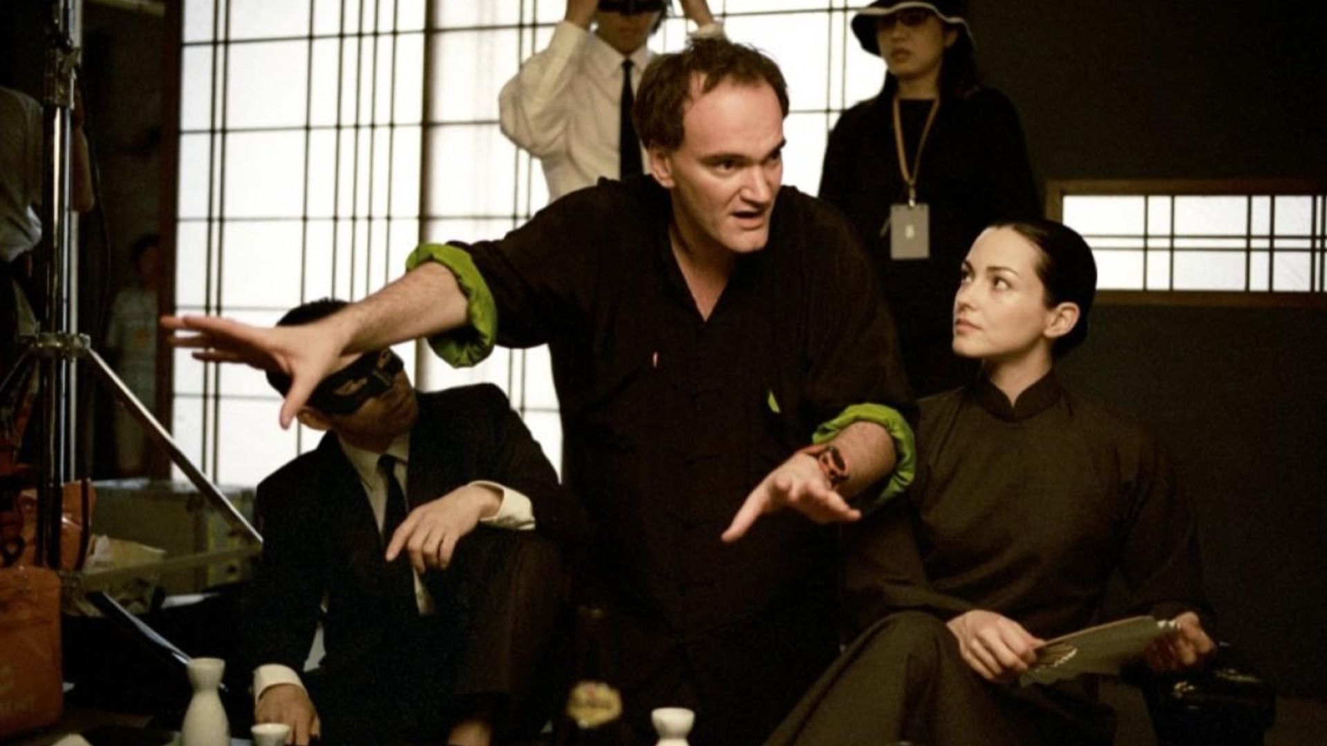 Regizorul Quentin Tarantino în haine negre dând indicații unor persoane în haine negre