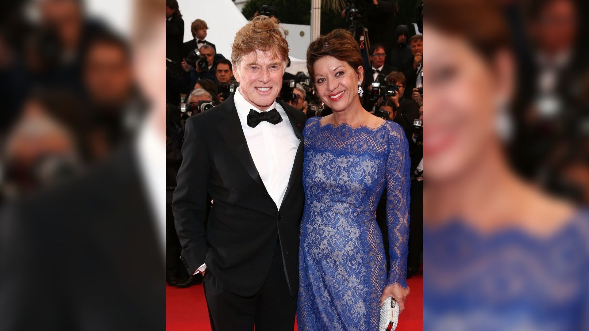 Robert Redford în smoking și Sibylle Szaggars într-o rochie albastră din dantelă pozează pe covorul roșu înconjurați de fotografi