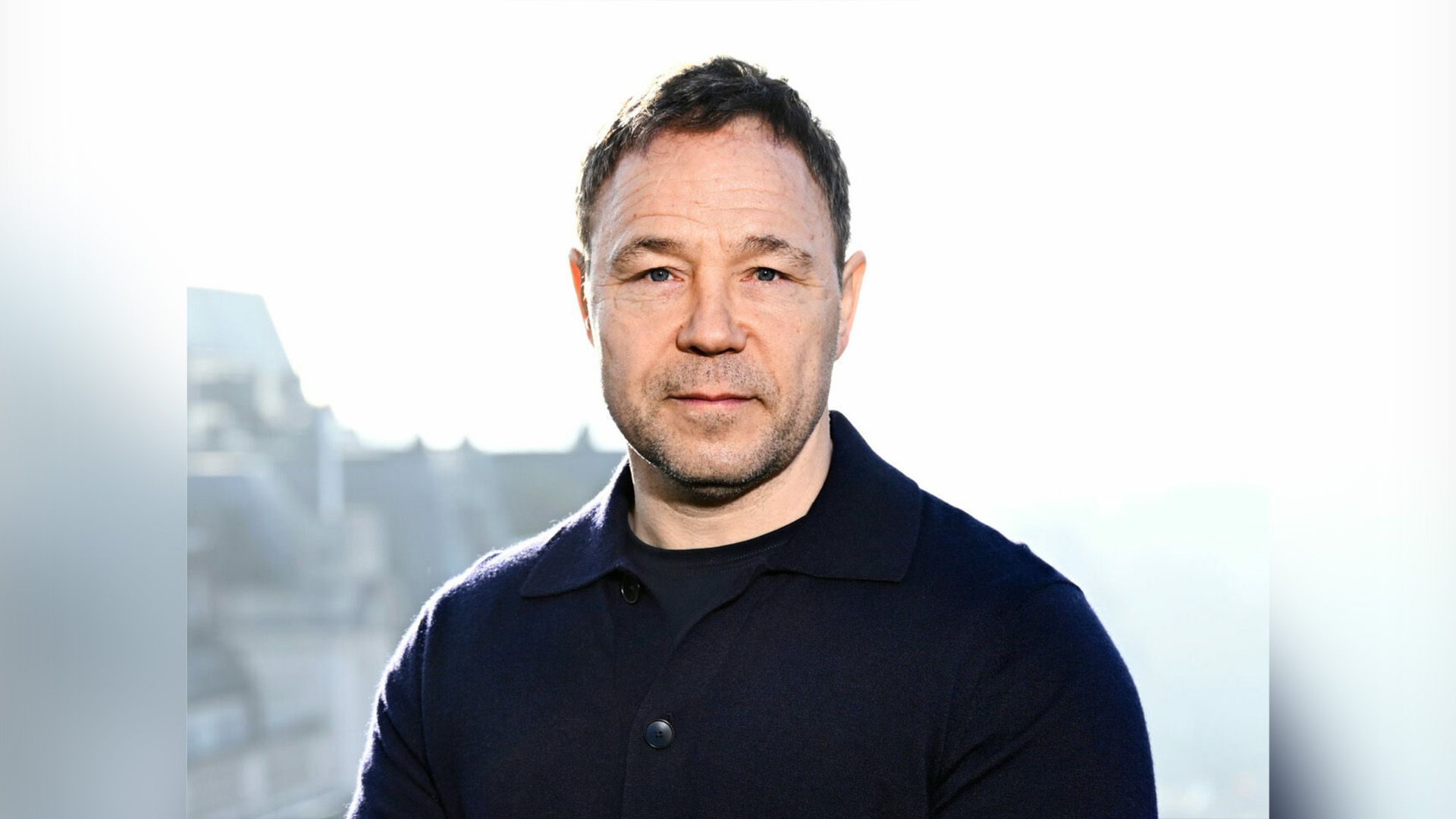 Actorul Stephen Graham într-un pulover negru pe fundal alb