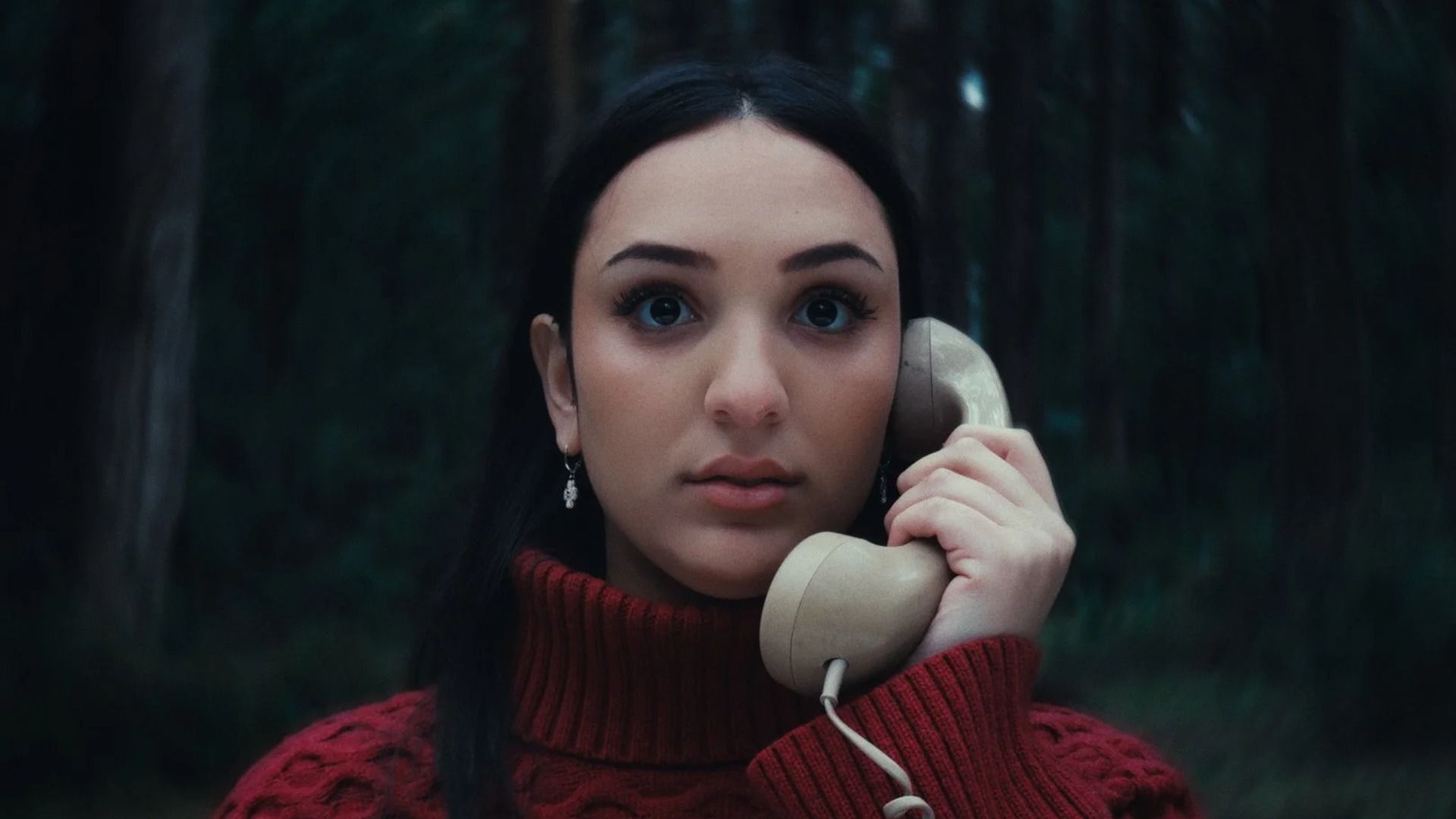 Fată în pulover roșu ținând un receptor de telefon stând în pădure