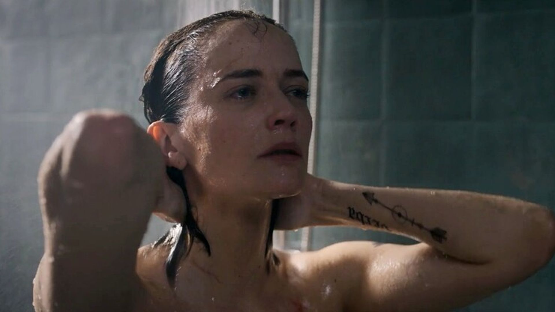 Eva Green cu părul ud făcând duș, mâinile în spatele capului, doar fața și brațul tatuaj vizibile