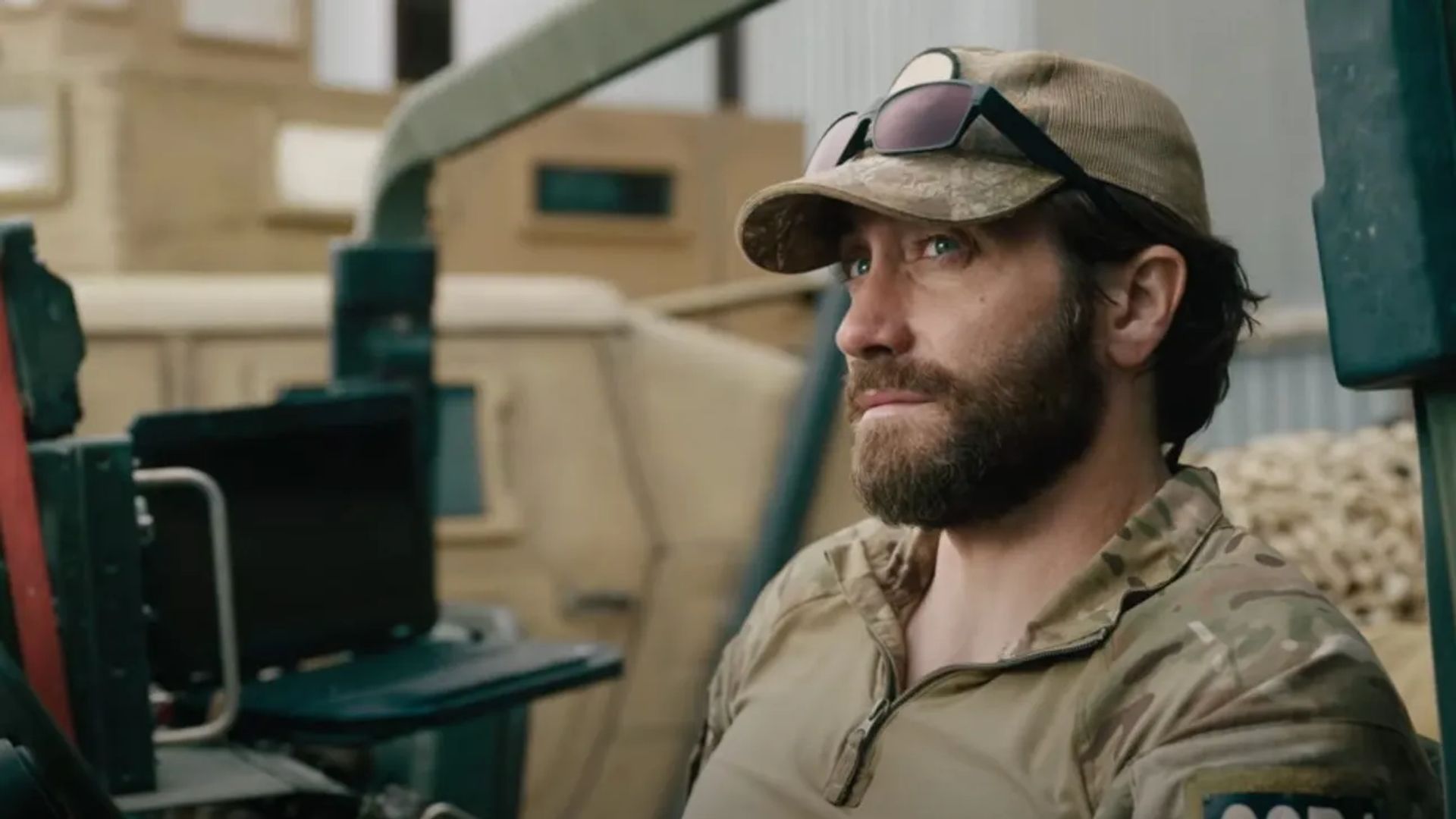 Jake Gyllenhaal în uniformă militară și șapcă cu ochelari pe vizieră stă privind într-o parte cu o expresie serioasă