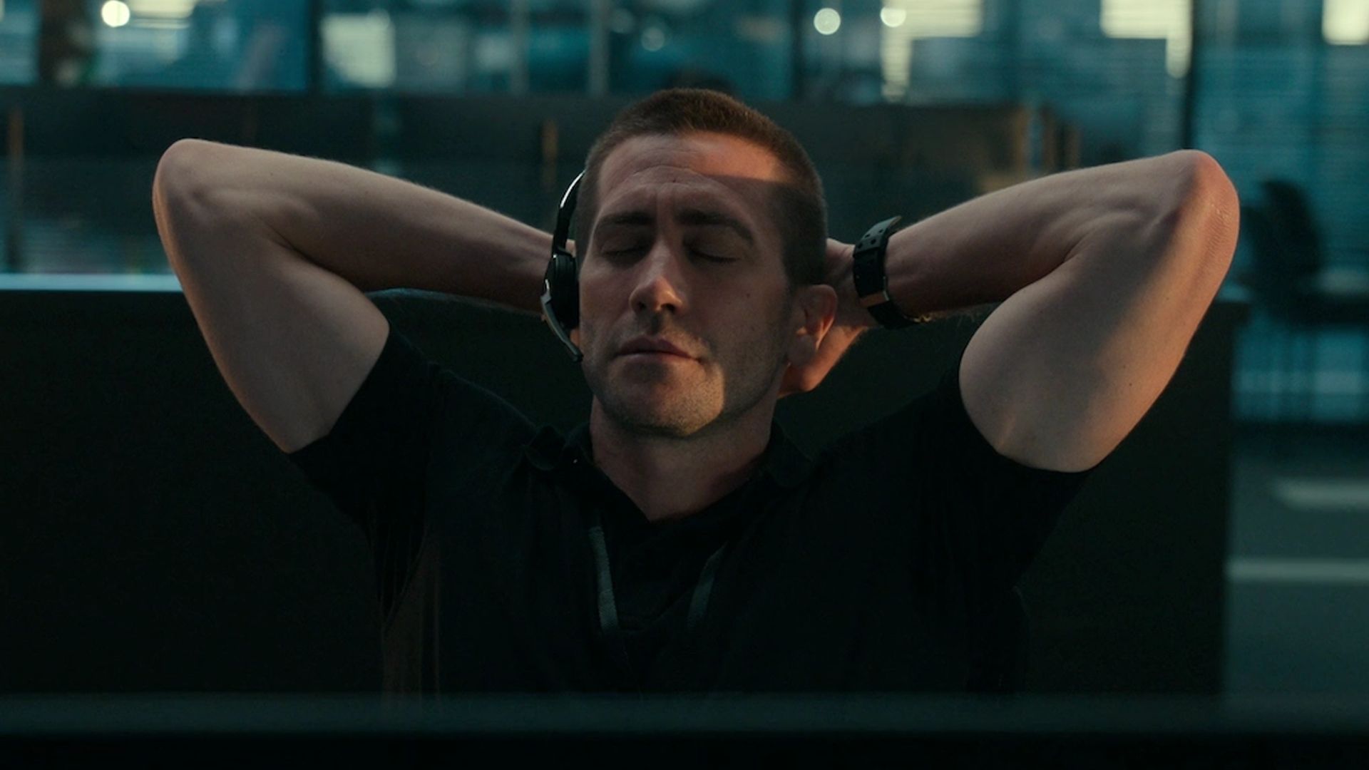 Jake Gyllenhaal purtând căști cu microfon stă cu ochii închiși, mâinile după cap