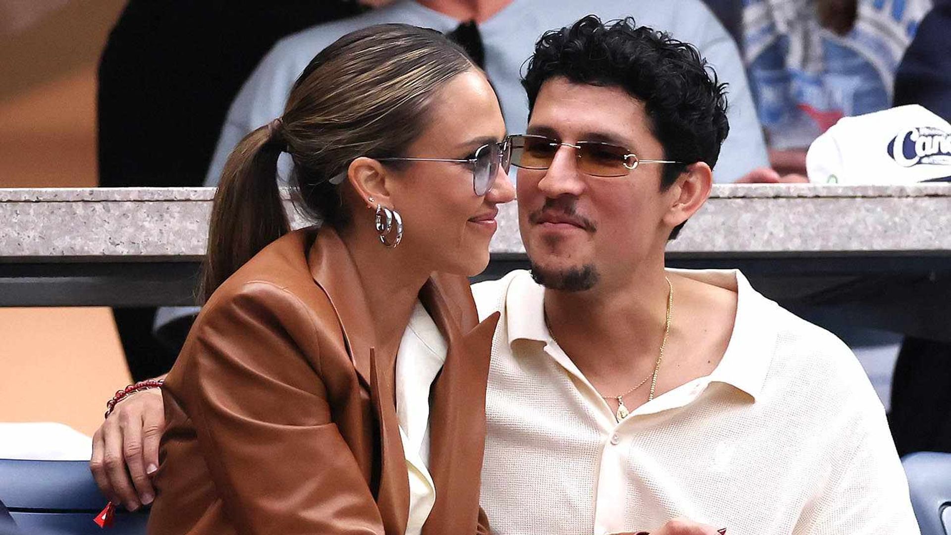 Jessica Alba și Danny Ramirez stând în tribună la un eveniment sportiv îmbrățișându-se