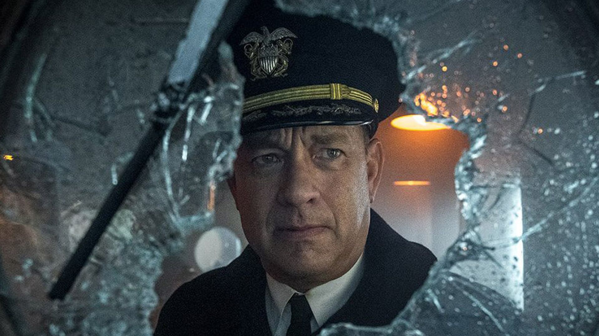 Tom Hanks în uniformă de căpitan se uită prin sticla spartă cu o expresie serioasă pe față