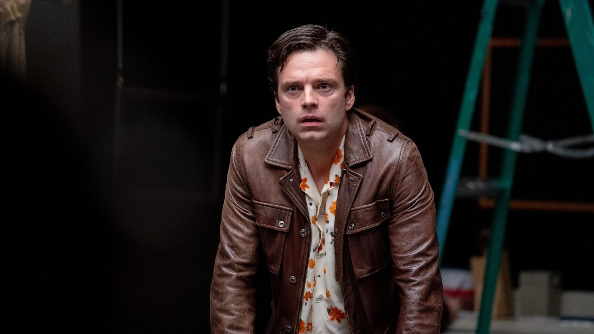 Sebastian Stan într-o jachetă maro privind înainte pe un fundal negru