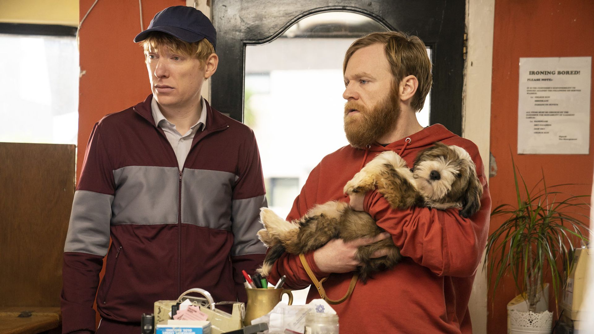 Brian și Domhnall Gleeson în ținută sport stând lângă o masă privind în lateral