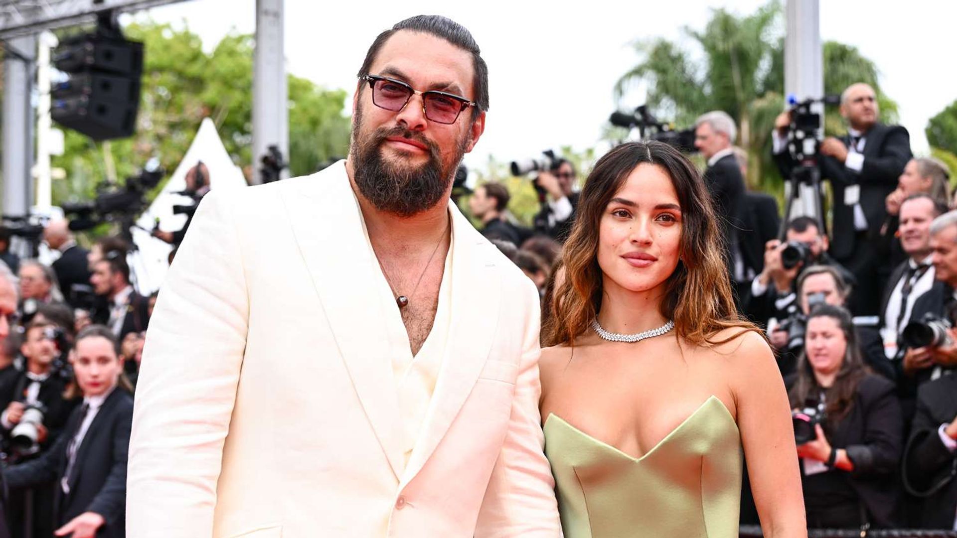 Jason Momoa în costum alb și Adria Arjona în rochie olive pe covorul roșu