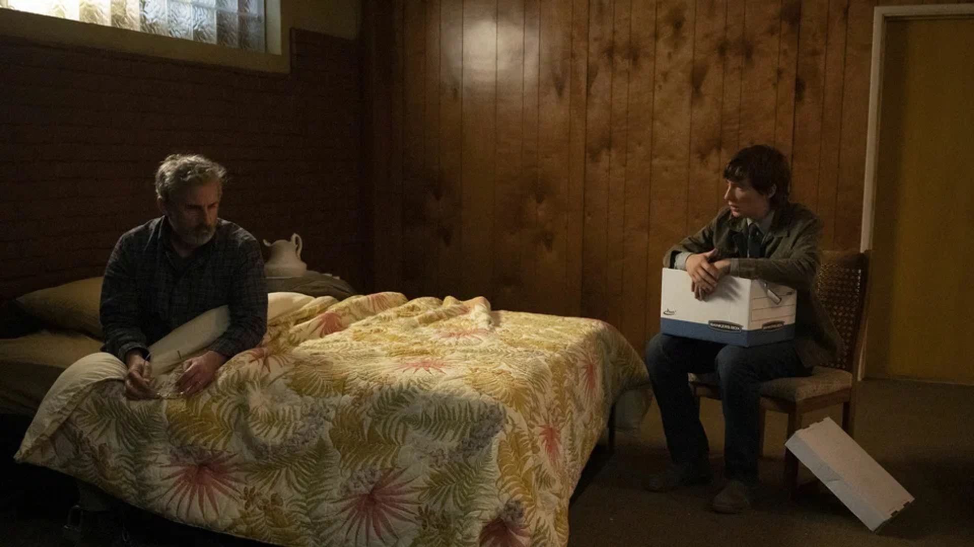 Steve Carell zăcând pe un pat cu Domhnall Gleeson șezând pe un scaun în fața lui